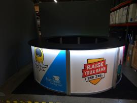 RENTAL: Modified RE-1226 Circular Counter with Black Laminated Top, Curved Locking Door, Black Laminated Shelving, Circular Carpeted Platform, and Direct Print Sintra Graphic Infill Panels.