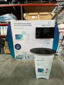 RENTAL: RE-1055 Segue Sunrise 10 x 10&rsquo; Design with (2) LED Arm Lights, Large Monitor Mount, 43 Inch Monitor, RE-1201 Tapered Counter, SEG Fabric Graphic, Direct Print Sintra Wing Graphics, and Vinyl Applied Counter Graphic