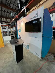 RENTAL: RE-1055 Segue Sunrise 10 x 10&rsquo; Design with (2) LED Arm Lights, Large Monitor Mount, 43 Inch Monitor, RE-1201 Tapered Counter, SEG Fabric Graphic, Direct Print Sintra Wing Graphics, and Vinyl Applied Counter Graphic