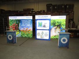 Custom Lightboxes with SEG Fabric Graphics, Full-size Locking Door, SYM-401 Backwall Workstation Counter, Wireless Charging Pad, (2) MOD-1381 Aluminum Literature Trays, (2) Monitor Mounts, and (2) SYM-407 Portable Counters with Locking Storage