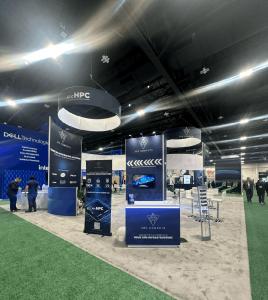 RENTAL: Modified RE-9097 Island Design with 16&rsquo; High Gravitee System Storage Tower, (2) 16 ft. High Curved Walls, (2) Curved Bridged Headers, (3) RE-1575 White Laminated Workstation Counters, (4) RE-1576 White Laminated Counters, (2) RE-703 Charging Sta