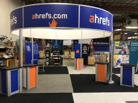 RENTAL: RE-9071 Island Design with 19&rsquo; Diameter Circular Header with Direct Print Sintra Infill Graphics, (6) RE-1219 Workstation Counters, RE-1228 Small Curved Counter, and Direct Print Sintra Infill Counter Graphics