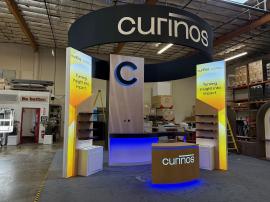 Custom ecoSmart Sustainable Island with Custom Reception, S-shape, and L-shape Counters, Monitor Mounts, Backlit Logos, SuperNova Lightboxes, Shelves, Locking Storage, Programmable LED RGB Lights, and Round Aero Header with Pillowcase Fabric Graphic