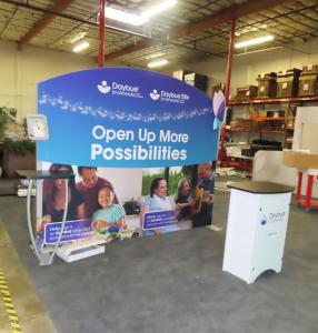 SYK-1026 Symphony Portable Display with SEG Fabric Graphic, Backwall Counter with Wireless Charging, Floating Graphic, MOD-1376 iPad Clamshell, LED Stem Lights, and SYM-406 Portable Counter with Locking Storage