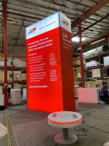 RENTAL: Island Design with Gravitee Storage Tower with Locking Door @ 100" Wide x 42" Deep x 190" High, Single-Sided Lightboxes on Front and Back of Tower, RE-1611 Waterfall Reception Counter with White Laminate Finish and Recessed RGB Accent Lighting, RE