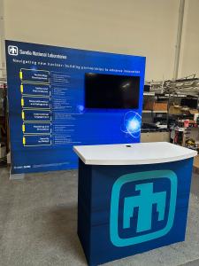 RENTAL: RE-1215 10&rsquo; x 10&rsquo; Inline Design with 110" Wide x 96" High Single-Sided Lightbox, Large Monitor Mount, 55" Monitor, RE-1558 Reception Counter, SEG Fabric Graphics