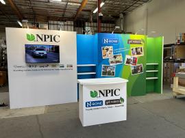 RENTAL: Inline Design with Gravitee Panel System Backwall, (6) 28" Wide x 10" Deep White Laminated Shelves, Large Monitor Mount, 43" Monitor, (6) LED Arm Lights, RE-1558 Gravitee Reception Counter, SEG Fabric Graphics