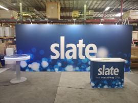 RENTAL: RE-2162 Inline Design with 232" Wide x 96" High Backwall, RE-1558 Gravitee Reception Counter, RE-704 Charging Station Table with Recessed RGB Accent Lighting, (5) LED Arm Lights, SEG Fabric Graphics, and Vinyl Applied Graphics